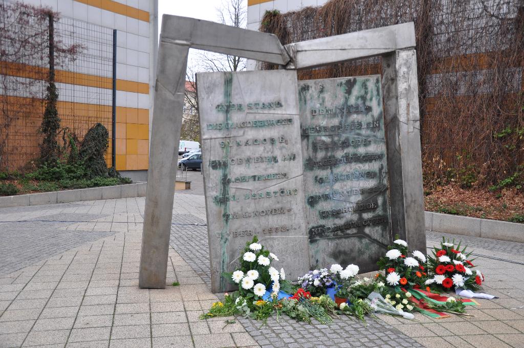 Mahnmal für die zerstörte Synagoge Magdeburgs: Zwei verwitterte Metalltafeln, die an antike Schrifttafeln erinnern. Davor niedergelegte Blumen.